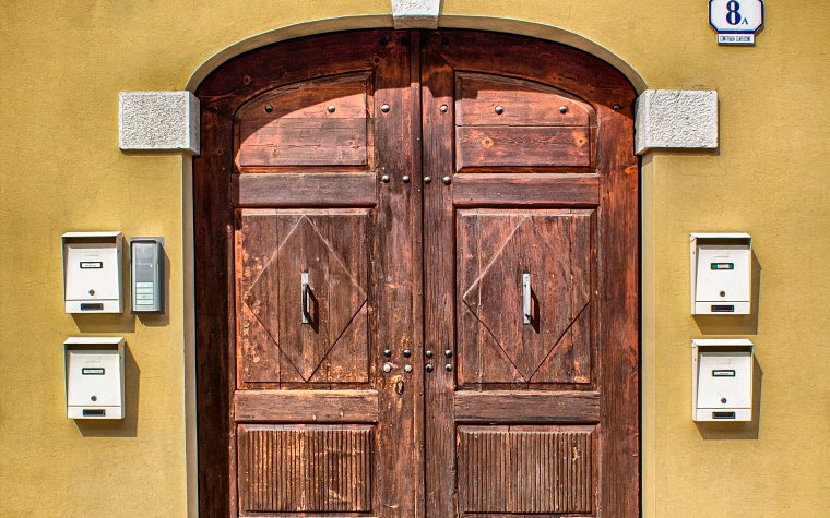 Portone di legno a due ante di un palazzo, con le cassette della posta e il citofono